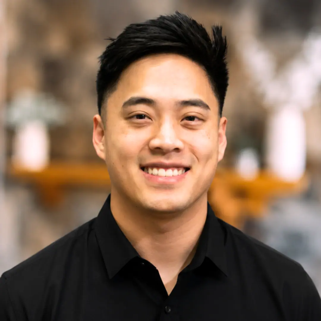 Smiling man in a black collared shirt posing for a professional headshot, blurred background