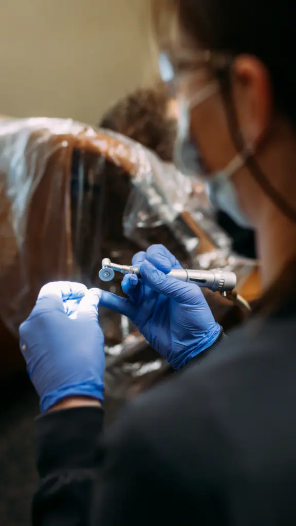 Dentist with blue gloves uses a dental handpiece over a patient during a procedure.