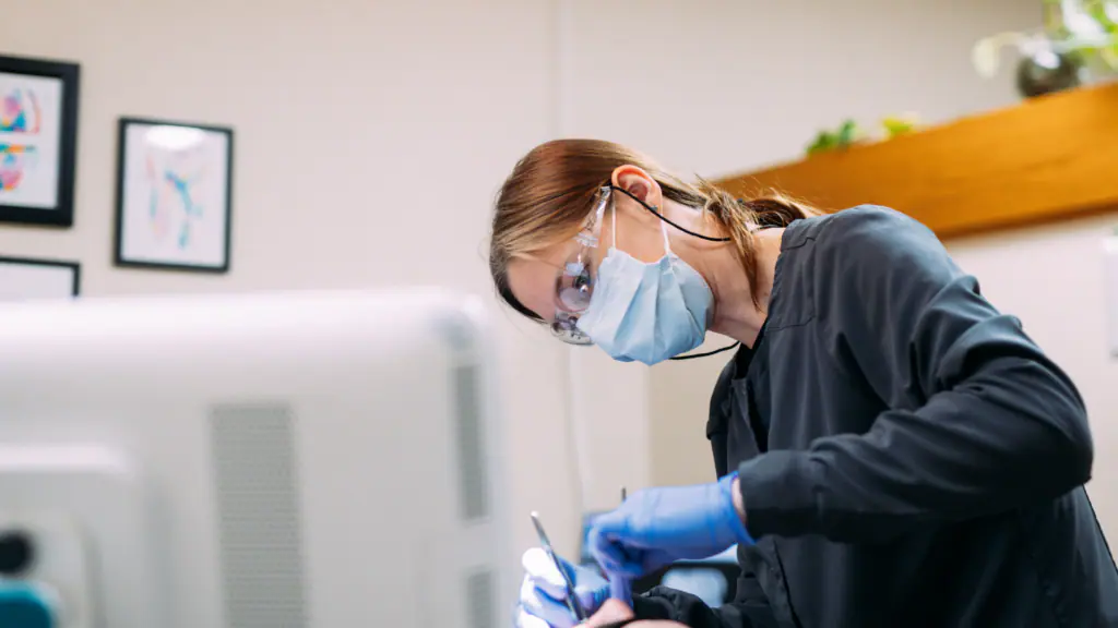 Healthcare worker in a mask, goggles, and gloves performing a procedure at a workstation.