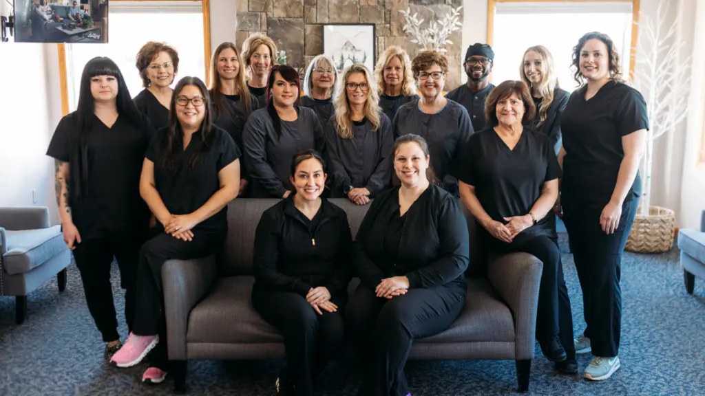 Group of healthcare workers in navy scrubs posing for a team photo in a lounge area with a stone fireplace behind them.