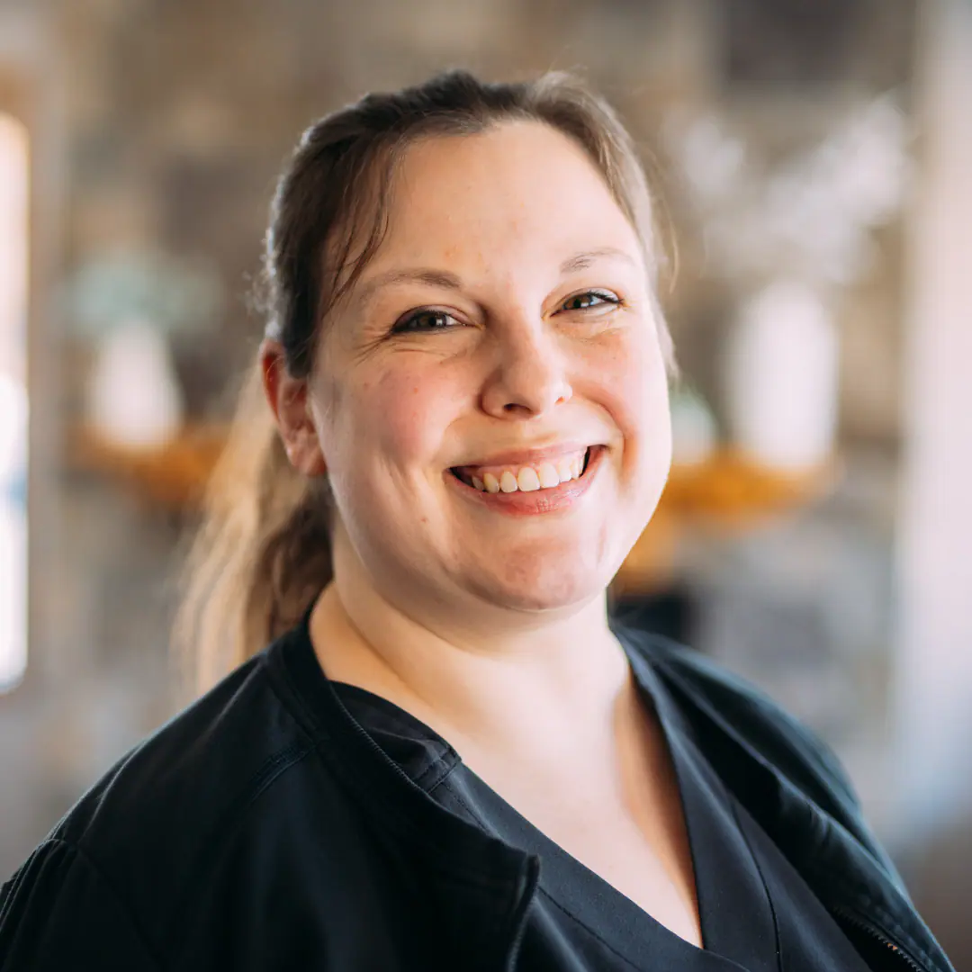 Portrait of a smiling woman in dark scrubs looking at the camera in a bright indoor setting.